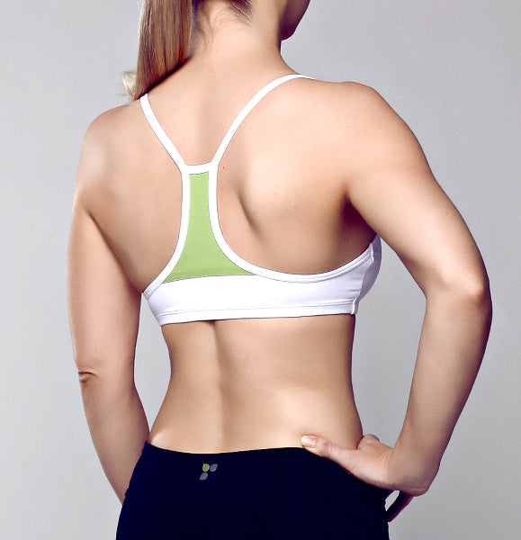 Back view of a woman wearing a white sport bra with green mesh inset fabric piece and black yoga pants