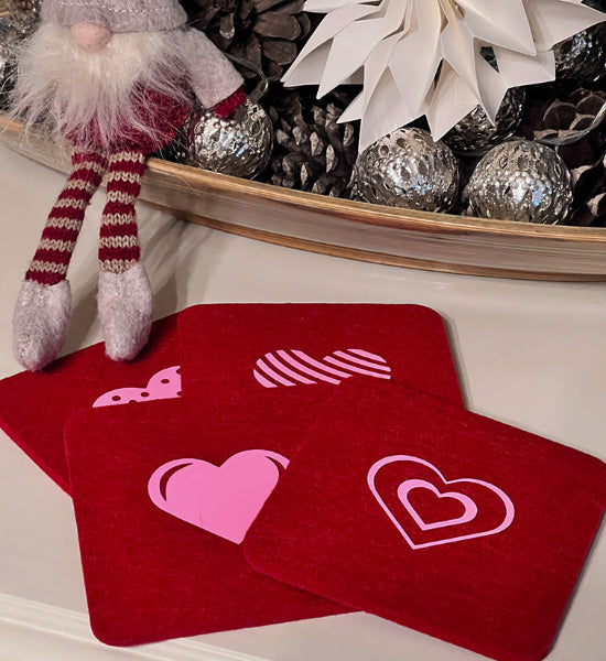 Product image of a set of four red wool coasters with pink decorative hearts heat transfers on a white table with festive decor