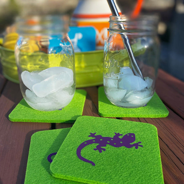 Closeup image of bright apple green wool drink coasters with purple animal designs and mason jars with ice and a stainless steel straw