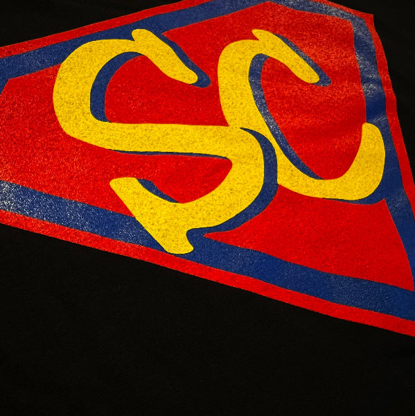 Closeup product detail image of a red graphic on a black knit fabric with the letters s and c printed in a red diamond shape