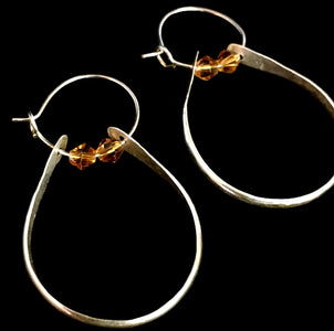 Closeup image of a pair of hammered sterling silver double hoop earrings with swarovski crystals on a black backgound