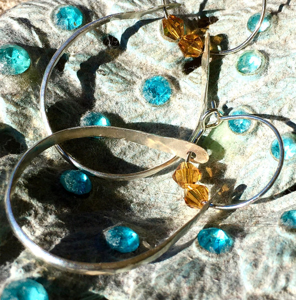 Closeup image of a pair of hammered sterling silver double hoop earrings with swarovski crystals on top of a ceramic and crystal bowl