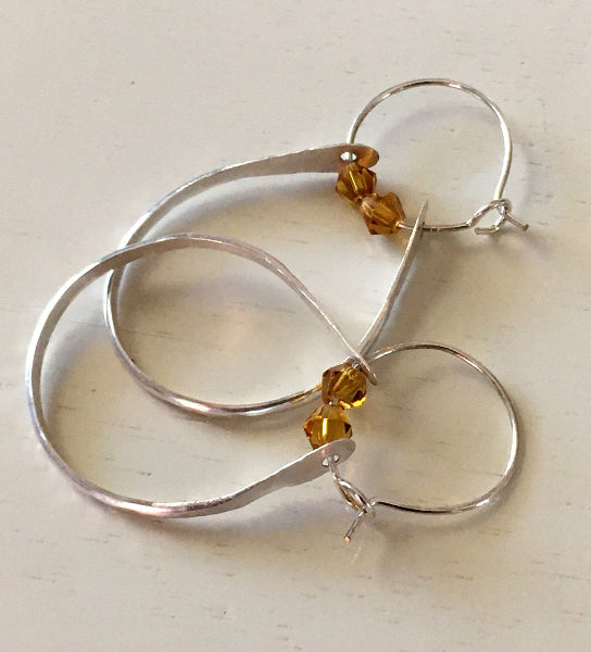 Closeup image of a pair of hammered sterling silver double hoop earrings with swarovski crystals on a white table