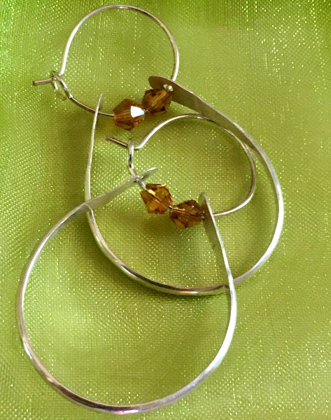 Closeup image of a pair of hammered sterling silver double hoop earrings with swarovski crystals on a green fabric background