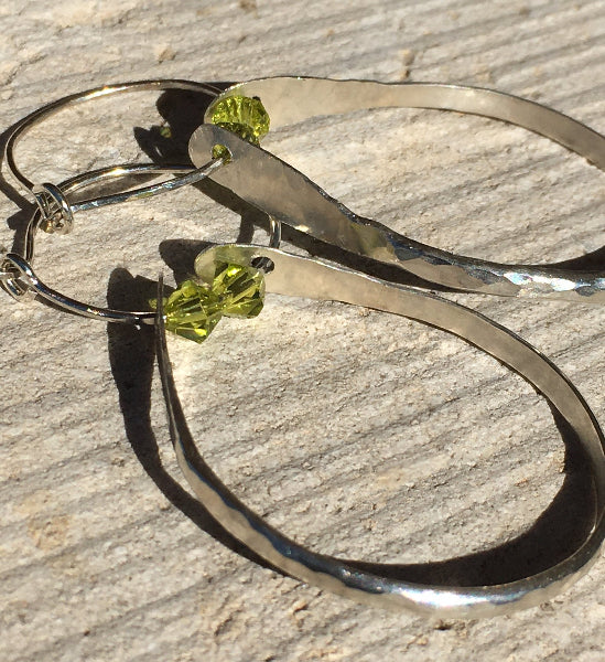 Closeup image of a pair of hammered sterling silver double hoop earrings with green swarovski crystals