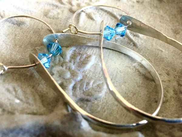 Closeup image of a pair of hammered sterling silver double hoop earrings with blue swarovski crystals