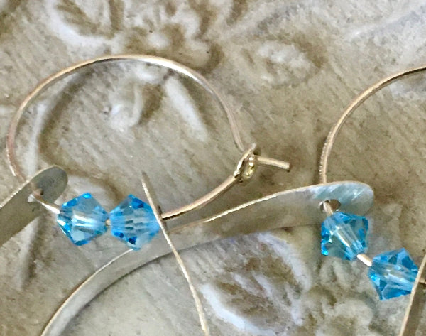 Closeup image of a pair of hammered sterling silver double hoop earrings with blue swarovski crystals