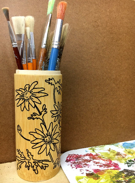 Image of a bamboo container with hand drawn black line art of daisies and artist paint brushes inside the container