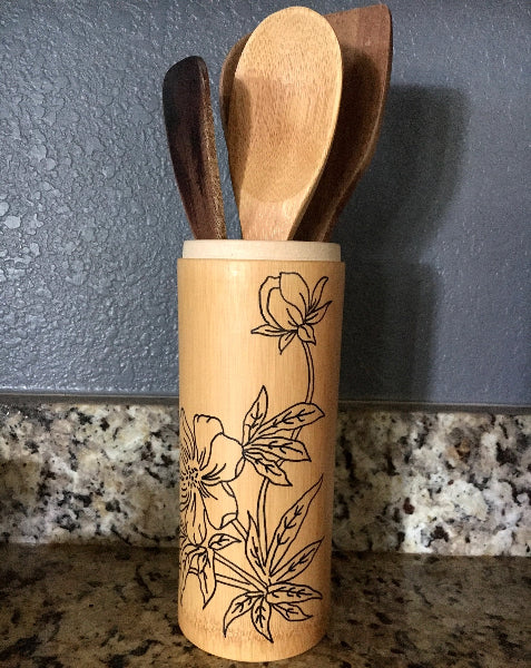 Image of a bamboo container with hand drawn black floral design and kitchen utensils on a countertop