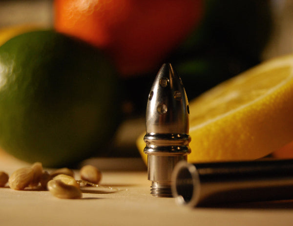 Closeup detail product image of stainless-steel metal seed trainer attachment for S'draw on a cutting board with sliced and whole citrus fruit and seeds