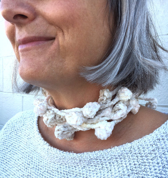 Closeup image of a woman wearing a grey sweater and a hand crocheted bobble chenille necklace