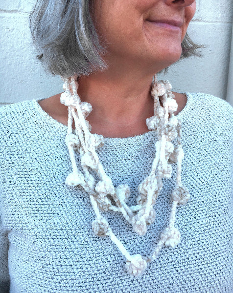 Closeup image of a woman wearing a grey sweater and a hand crocheted bobble chenille necklace