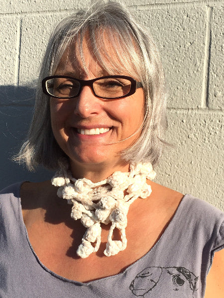 Closeup image of a woman wearing glasses and a grey t-shirt and a hand crocheted bobble chenille necklace