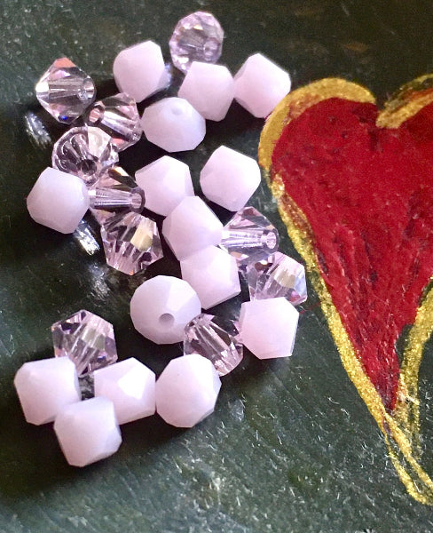 Closeup image of pink swarovski crystal beads on a grey background with a hand painted red heart