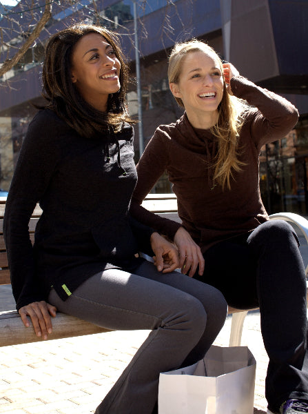 Image of two women sitting on a park bench, smiling, wearing black and brown tunic tops and grey and black boot cut yoga pants