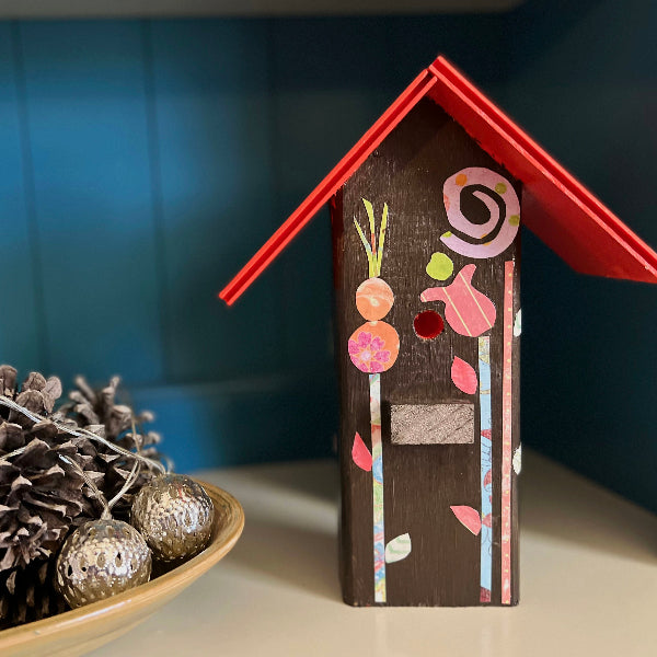 Front view of a decorative wooden birdhouse with a red roof and decoupaged floral design inside of a blue hutch