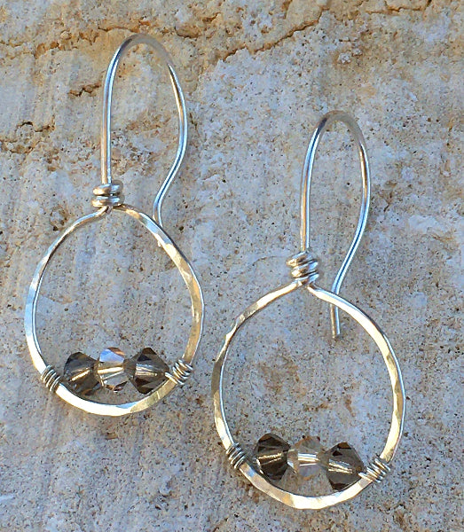 Closeup image of hammered sterling silver forward-facing hoop earrings with silver wire wrap and swarovski crystals