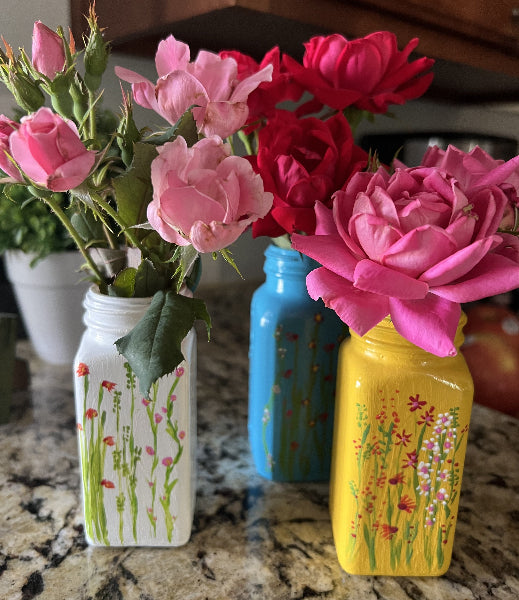 Closeup image of three hand painted small bud vases with floral painting on the front and filled with roses