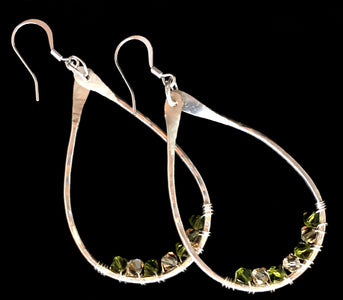 Closeup image of a pair of hammered sterling silver teardrop hoop earrings with silver wire wrap and swarovski crystals on a black background