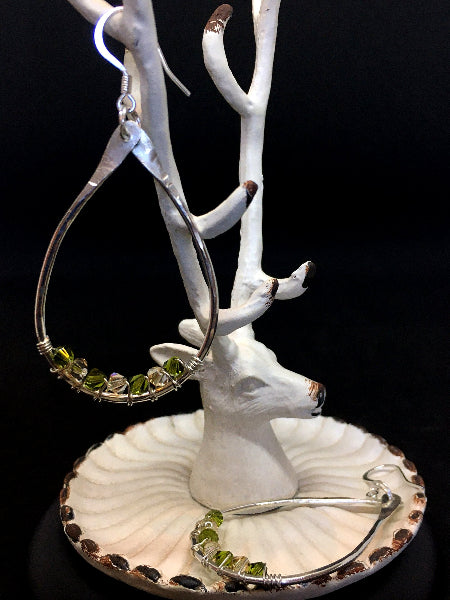 Closeup image of a pair of hammered sterling silver teardrop hoop earrings with silver wire wrap and swarovski crystals hanging from antlers of a deer shaped white jewelry tree