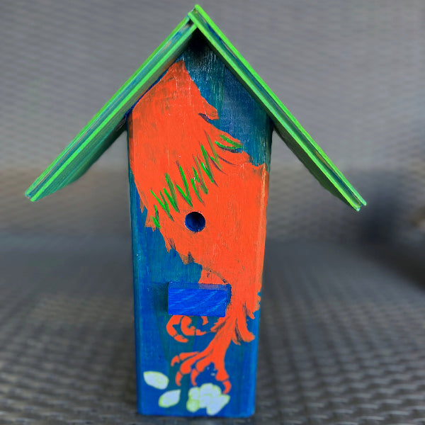 Product image of a blue hand painted wood decorative birdhouse with an orange rooster painted on the front and a green roof on top of a wicker chair