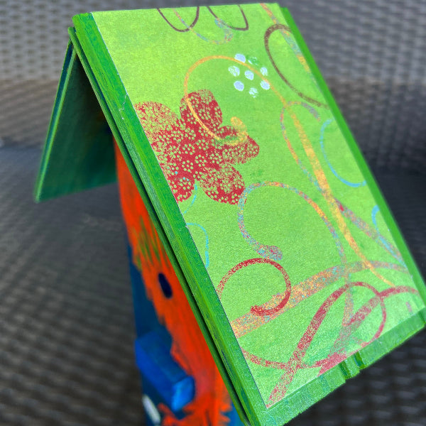 Closeup image of a green patterned floral decoupaged roof on a wooden decorative birdhouse