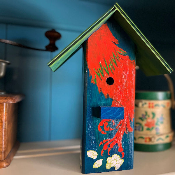 Closeup image of a hand painted blue decorative wooden birdhouse with a green roof and an orange rooster painted on the front