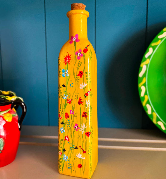 Closeup front view image of a small bud vase hand painted yellow with small flowers painted on the front standing in front of a blue painted wood background