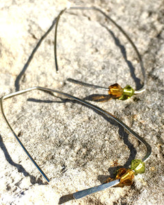 Closeup image of a pair of hammered sterling silver rectangle hoop earrings with swarovski crystals laying on top of a piece of limestone