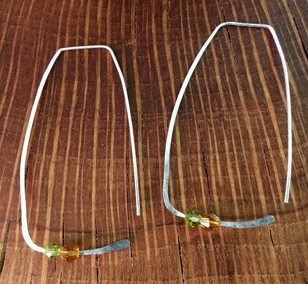 Closeup image of a pair of hammered sterling silver rectangle hoop earrings with swarovski crystals displayed on a piece of wood