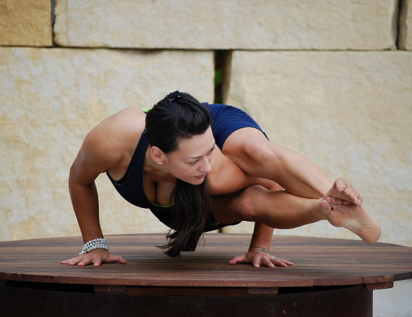 Image of a yoga instructor practicing yoga on a wooden platform in front of a limestone wall, wearing navy blue yoga clothes