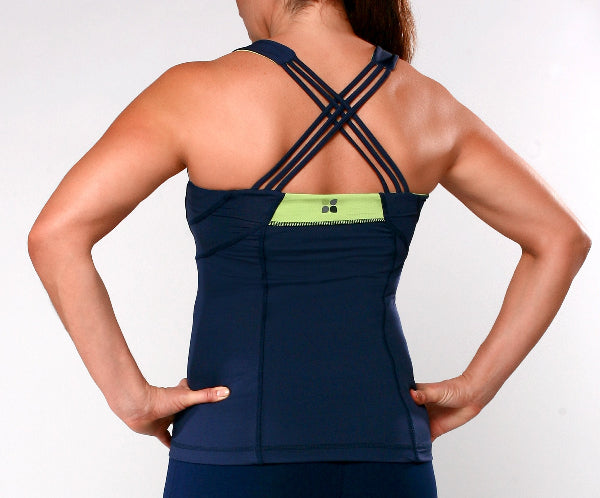 Closeup back view image of a woman wearing a navy blue strappy yoga tank top with seams and a bright green mess inset in the back