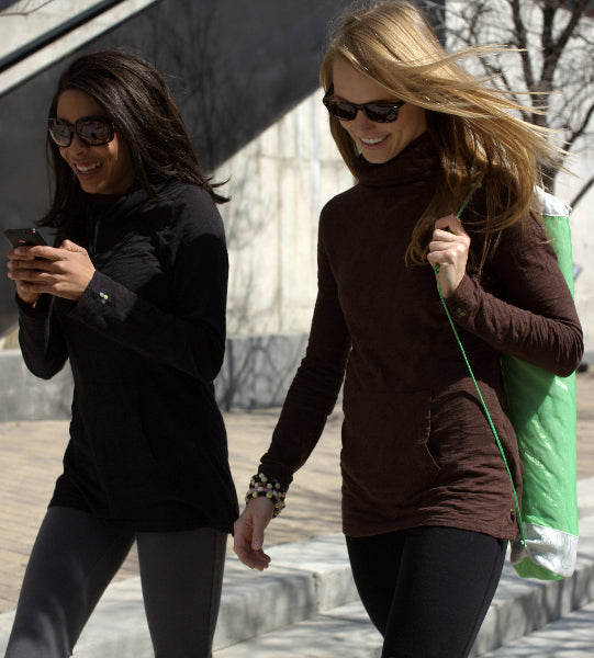 Image of two women, wearing sunglasses, walking in front of a building, smiling and wearing long sleeve organic cotton slubbed tunic tops in Black and chocolate brown and grey and black yoga pants