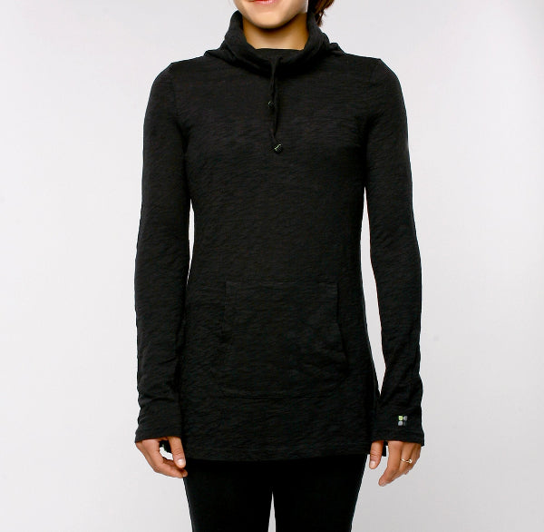 Front view image of a woman wearing a long sleeve slubbed organic cotton black fitted tunic top with flared sleeves, a mock turtleneck with drawcords, front kangaroo pocket and black yoga pants