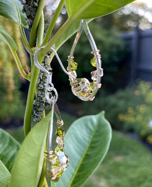 Image of a pair of hammered sterling silver earrings with gold wire wrap and swarovski crystals hanging from a plant in a garden