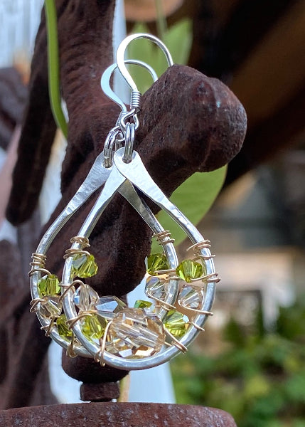 Product image of a pair of hammered sterling silver teardrop earrings with gold wire wrap and swarovski crystals hanging on a rustic post