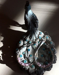 Closeup image of a pair of hammered sterling silver teardrop hoop earrings with silver wire wrap and swarovski crystals on top of a ceramic peacck shaped jewelry dish