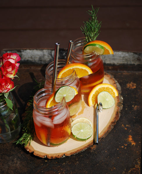 Top front view of three mason jars with sweet tea, lemon slices, rosemary sprig and stainless=steel metal straws on a wood tray