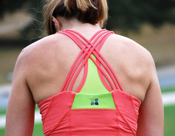 Closeup back view of a woman wearing a form fitting coral orange color strappy yoga tank top over a sport bra