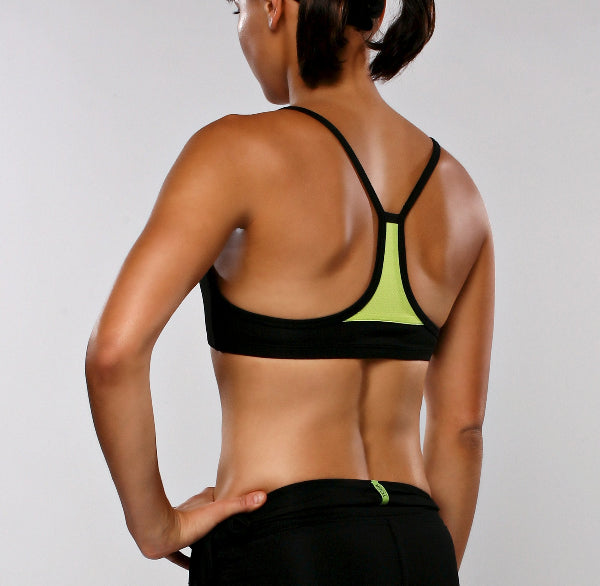 Back view of a female athlete model wearing a black sport bra with bright apple green mesh and black running shorts