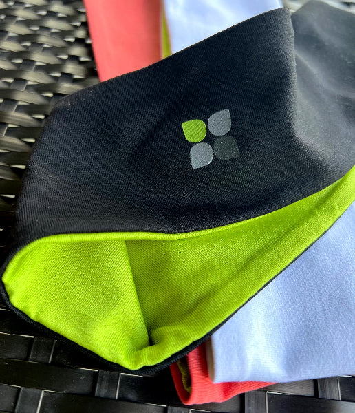 Closeup product image of a black wide headband with bright green fabric inside of the headband and a Yoga City logo printed on the outside on top of a black wicker table