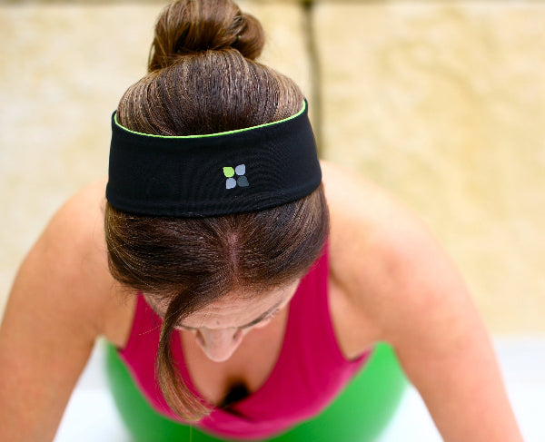 Closeup image of a woman doing yoga wearing a fuchsia color tank top and a black wide headband with a Yoga City brand logo on the front