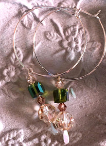 Closeup image of a pair of hammered sterling silver wire hoop earrings with dangling swarovski crystals on a ceramic floral design dish