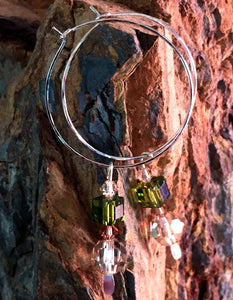 Closeup image of a pair of hammered sterling silver wire hoop earrings with dangling swarovski crystals hanging from a piece of petrified wood