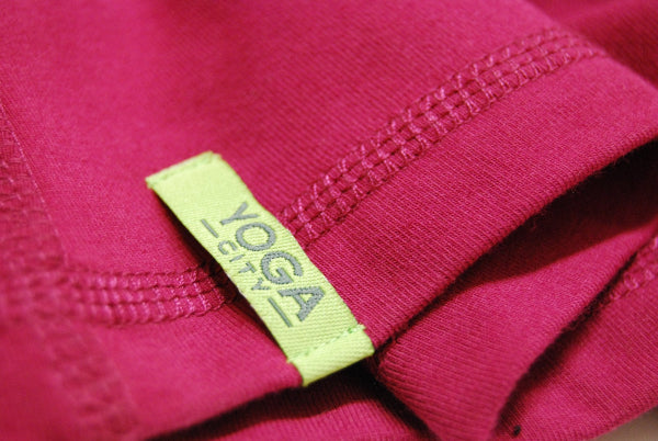 Extreme closeup detail image of the bottom hem of a wine color yoga tank top with a bright green label with the words Yoga City on it