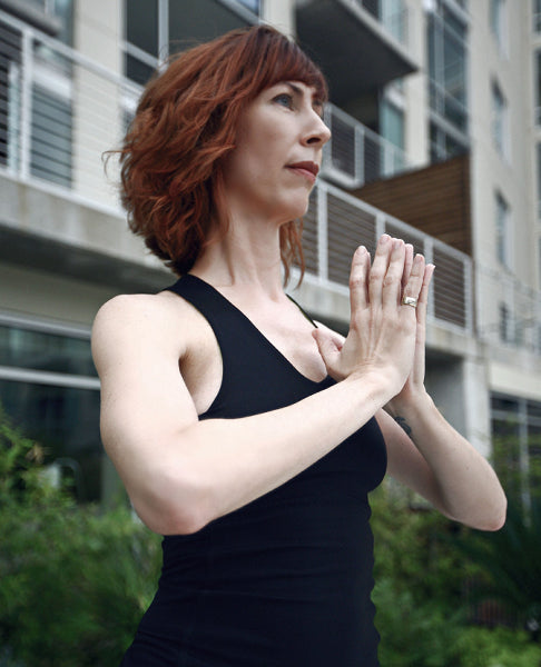 Closeup side view image of a woman practicing yoga in front of an apartment building, wearing a black yoga tank top